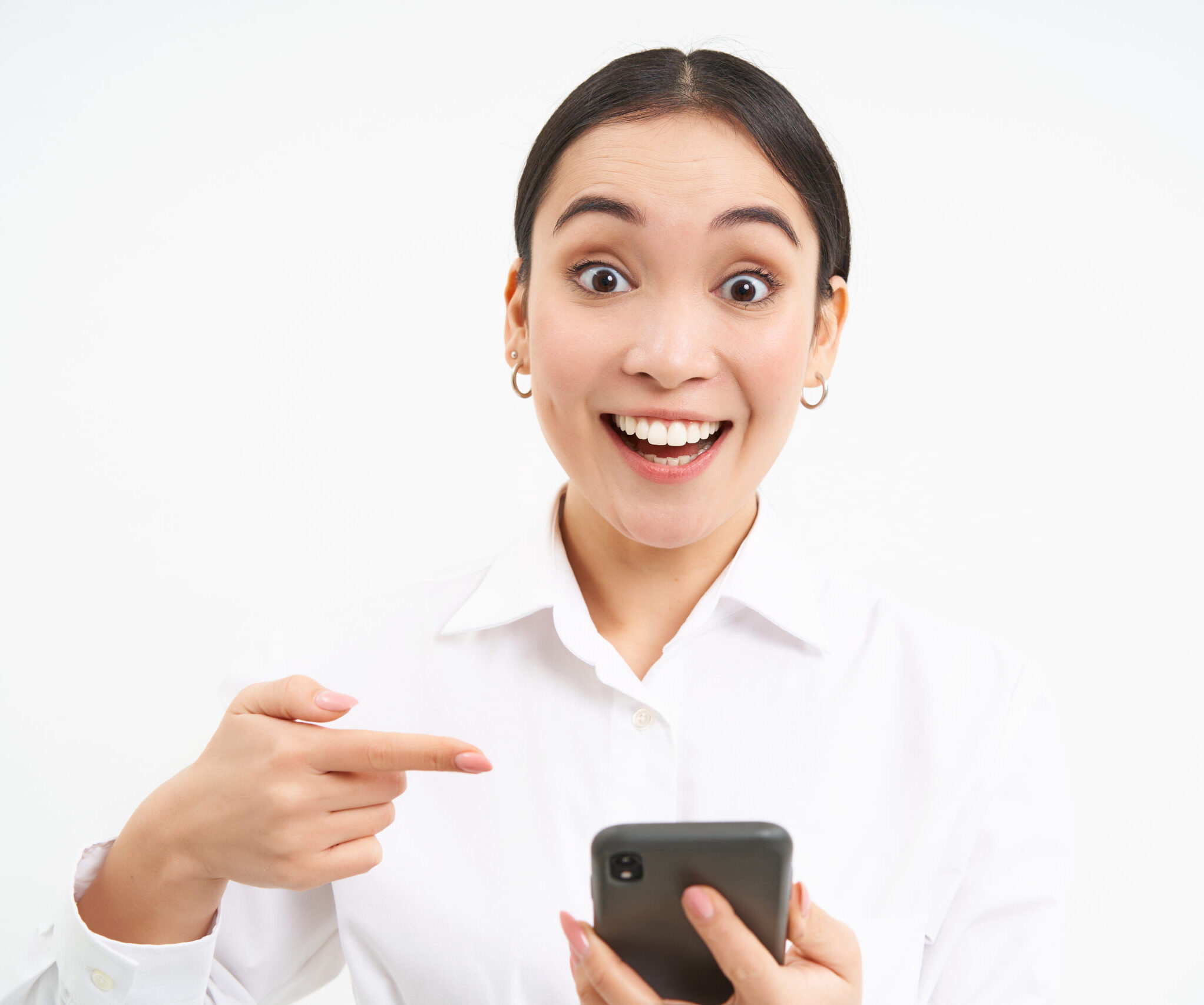Close up portrait of happy saleswoman, successful woman with smartphone, pointing at her phone and smiling amazed, standing over white background.